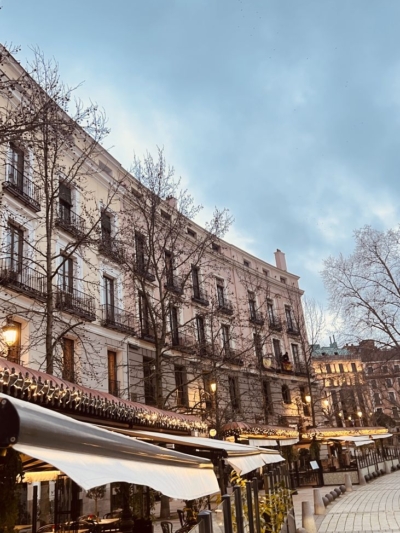 Atmospheric street in Madrid with neoclassical buildings and warmly lit restaurants, captured during a sourcing trip for Guanabana products for The Little Store in Pythagoreio, Samos